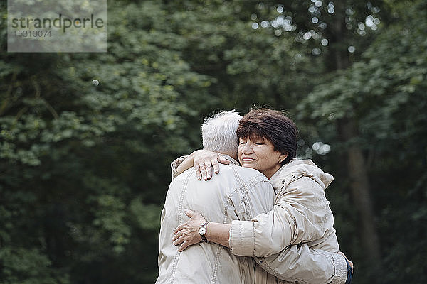 Porträt einer älteren Frau  die ihren Mann im Wald umarmt