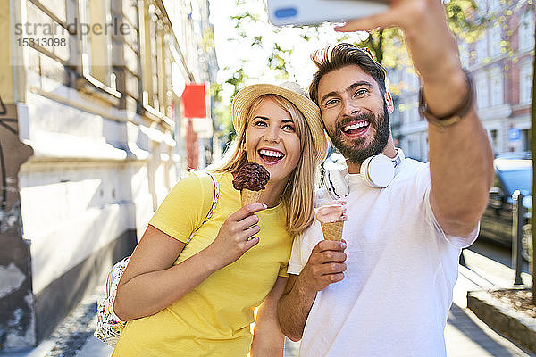 Glückliches junges Paar  das sich beim Eisessen in der Stadt ein Selfie gönnt