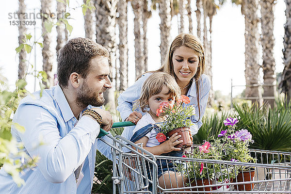 Eine Familie kauft Pflanzen in einem Gartencenter  während die Tochter im Einkaufswagen an einer Blume riecht
