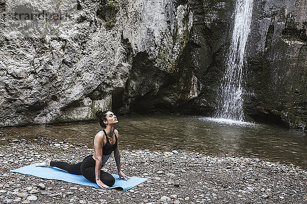 Frau praktiziert Yoga am Wasserfall  Kobra-Pose