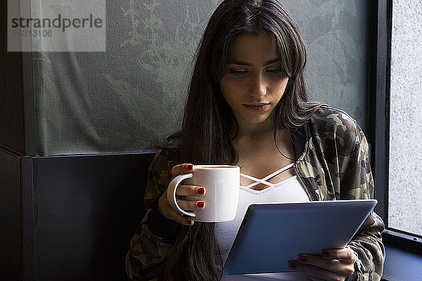 Junge Frau sitzt im Café mit einer Tasse Kaffee und benutzt Tabletten