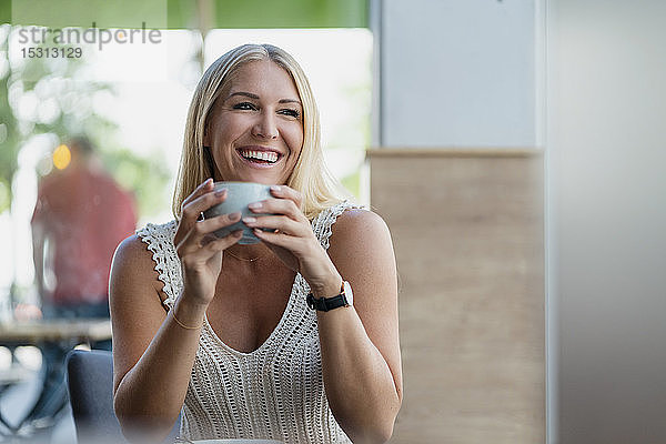Porträt einer glücklichen blonden Frau  die in einem Café Kaffee trinkt