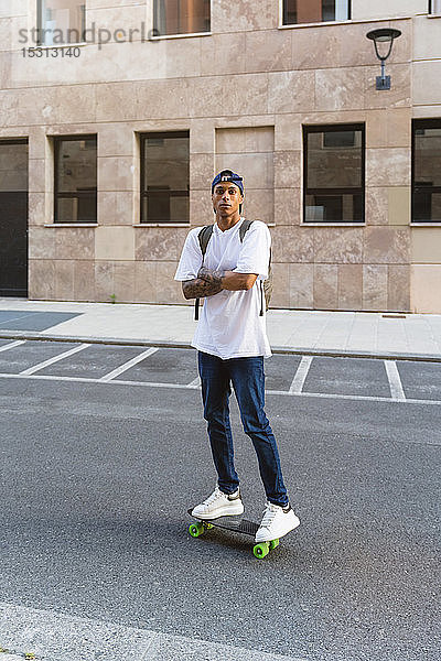 Porträt eines tätowierten jungen Mannes auf einem Skateboard stehend