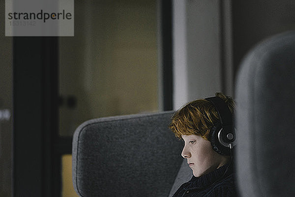 Profil eines rothaarigen Jungen mit Kopfhörern auf einem Ohrensessel