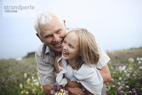 Lachender Grossvater und Enkelin mit gepflückten Blumen auf einer Wiese