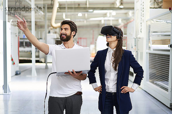 Mann mit Laptop und Geschäftsfrau mit VR-Brille in der Fabrik