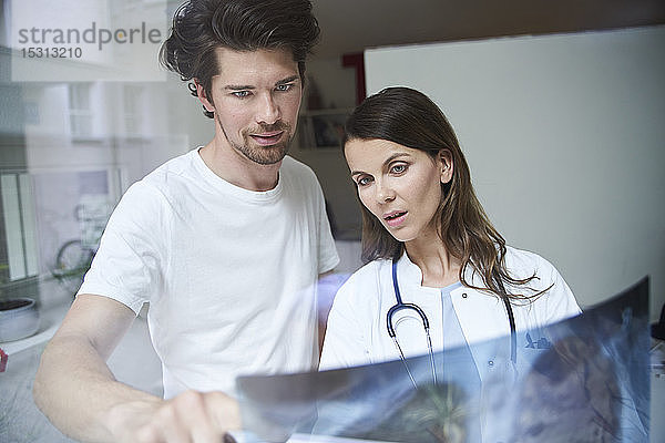 Zwei Ärzte mit Röntgenbild hinter Fensterscheibe