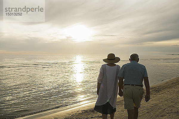 Rückenansicht eines älteren Ehepaares  das bei Sonnenuntergang Hand in Hand am Strand spazieren geht  Liepaja  Lettland