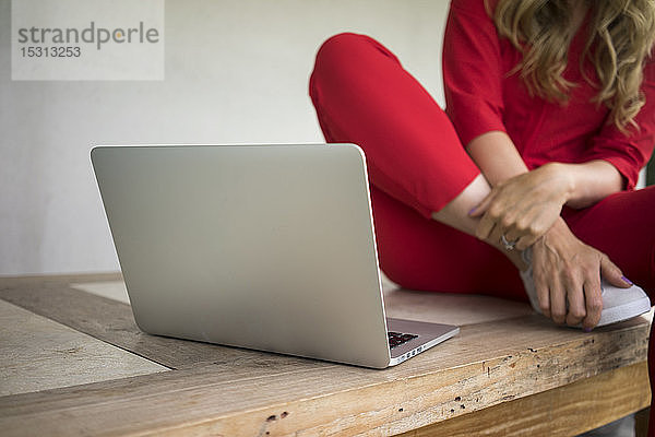Nahaufnahme einer Frau mit Laptop  die zu Hause auf einem Holztisch sitzt