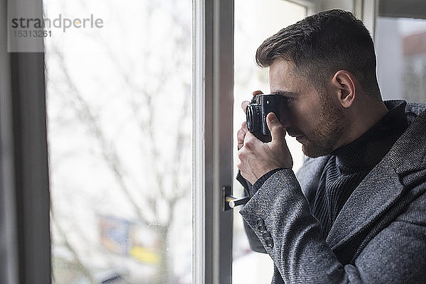 Junger Mann beim Fotografieren am Fenster