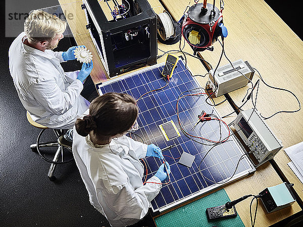 Zwei Techniker arbeiten im Labor an 3D-gedrucktem Turbinenrad und Solarpanel