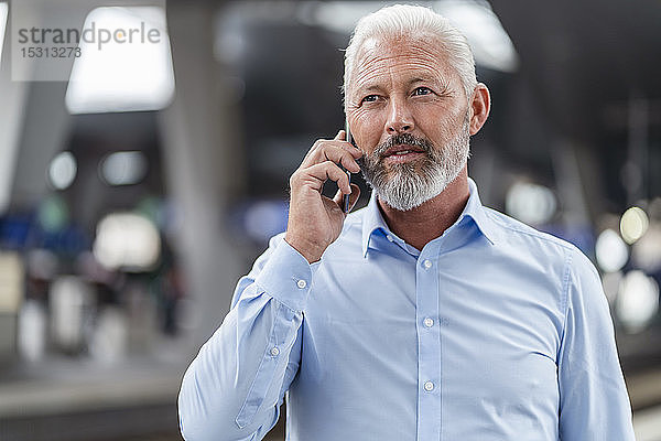 Ein reifer Geschäftsmann telefoniert am Bahnsteig mit einem Mobiltelefon
