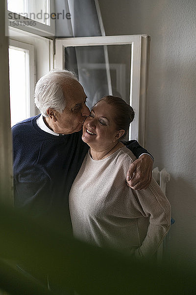 Glückliches älteres Paar küsst sich zu Hause am Fenster