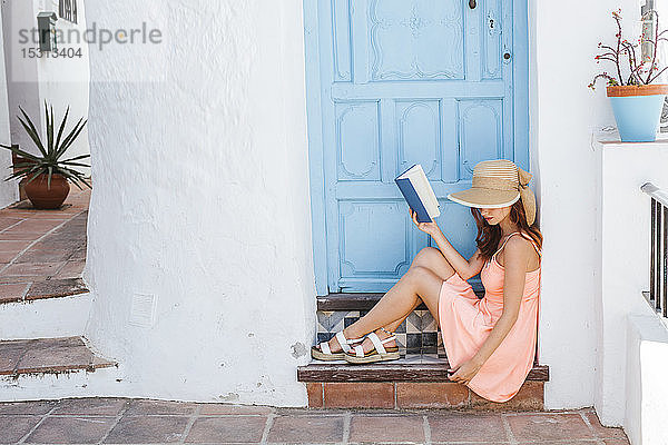 Junge Frau mit Buch auf der Stufe des Hauseingangs sitzend  Frigiliana  Málaga  Spanien