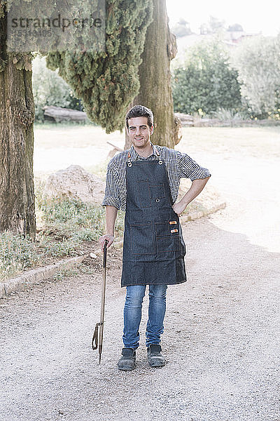 Porträt eines selbstbewussten Junglandwirts  der ein Werkzeug auf einem Feldweg hält