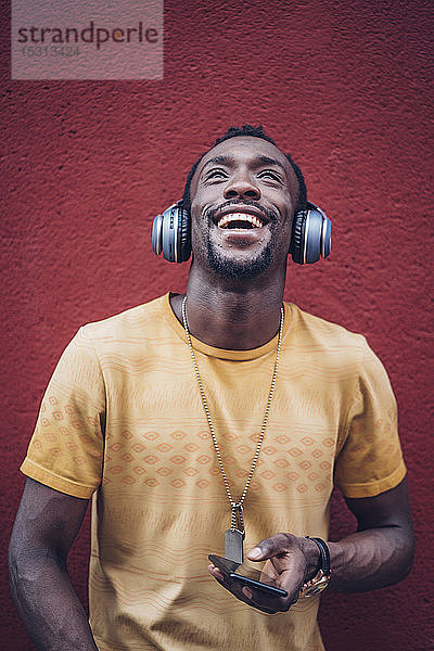 Porträt eines glücklichen Mannes mit Kopfhörer und Smartphone  der nach oben schaut