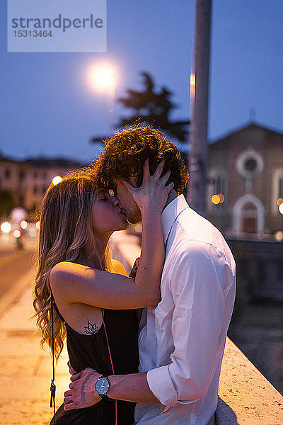 Zärtliches junges Paar küsst sich nachts auf einer Brücke  Verona  Italien