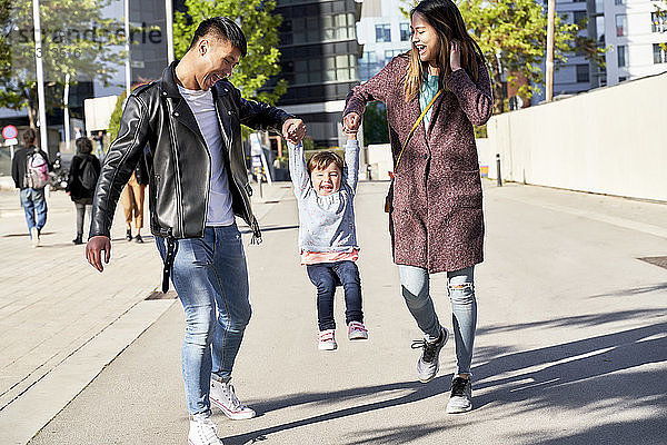 Glückliche Eltern halten ein kleines Mädchen beim Springen an der Hand  Barcelona  Spanien