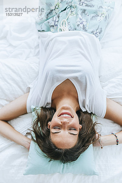 Draufsicht auf eine glückliche junge Frau  die mit geschlossenen Augen im Bett liegt