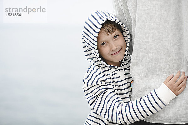 Porträt eines lächelnden Jungen mit gestreifter Kapuzenjacke  der seinen Vater umarmt