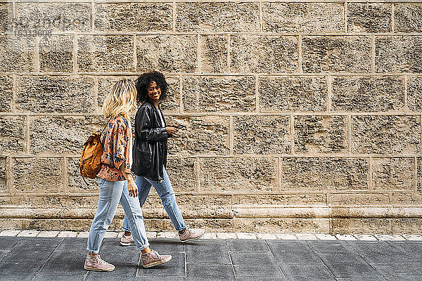 Multikulturelle glückliche Frauen  die in der Stadt spazieren gehen und ein Smartphone benutzen