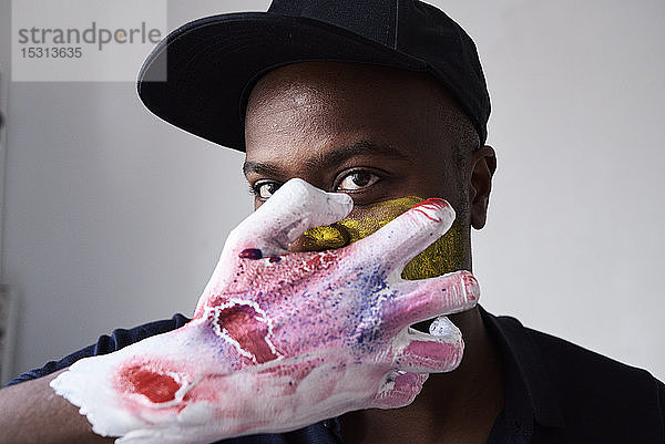 Wütende Künstlerin mit einer mit Farbe bedeckten Hand  die in die Kamera schaut