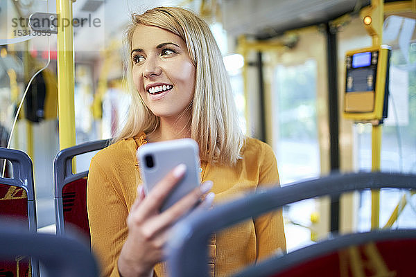 Lächelnde junge Frau mit Smartphone in einer Straßenbahn