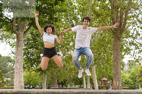 Junges Paar springt im Park von einer Mauer