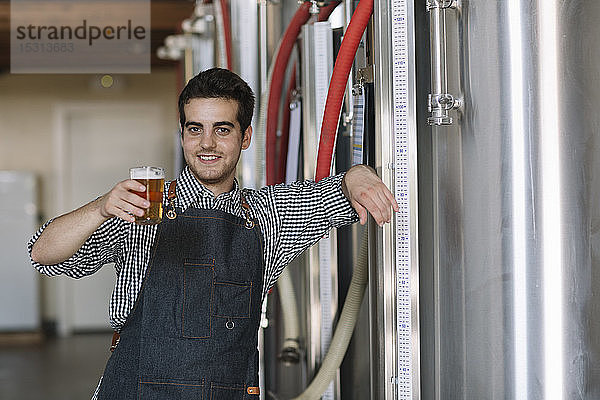 Porträt eines selbstbewussten jungen Mannes mit Bierglas in der Hand in einer Brauerei