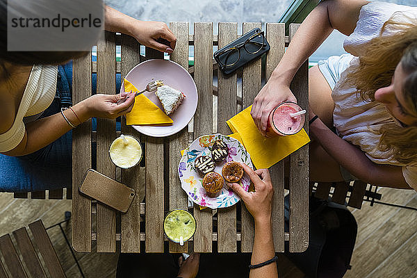 Draufsicht auf drei junge Frauen  die an einem Holztisch mit Smoothies und Keksen sitzen