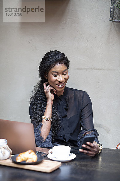 Lächelnde schicke Geschäftsfrau mit Smartphone am Tisch in einem Café
