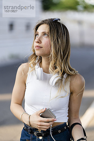 Porträt einer jungen Frau mit Kopfhörer und Smartphone nach oben schauend