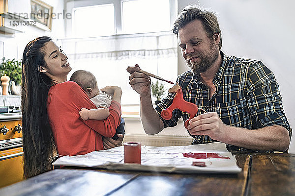 Familie malt Holzspielzeugpferd für Baby am Küchentisch zu Hause