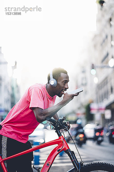 Junger Mann mit E-Fahrrad und Kopfhörer mit Smartphone in der Stadt