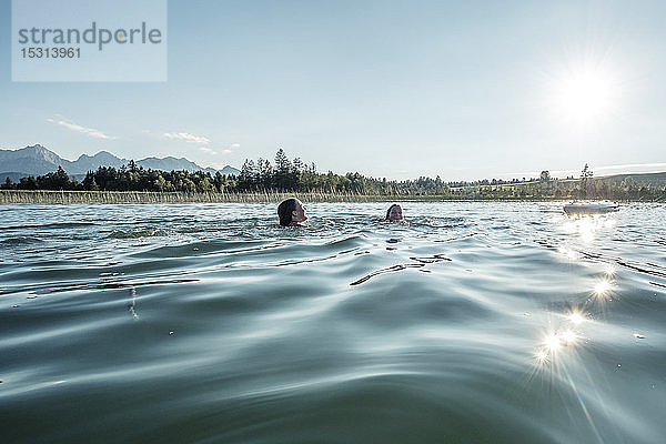 Zwei Mädchen schwimmen bei Sonnenschein in einem See  Bannwaldsee  Allgäu  Bayern  Deutschland