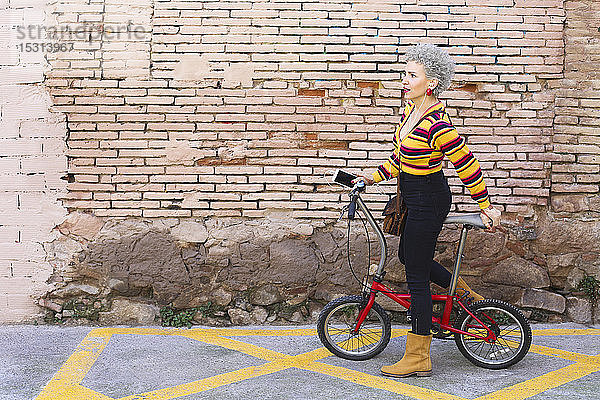 Modische reife Frau mit Fahrrad und Smartphone auf der Straße