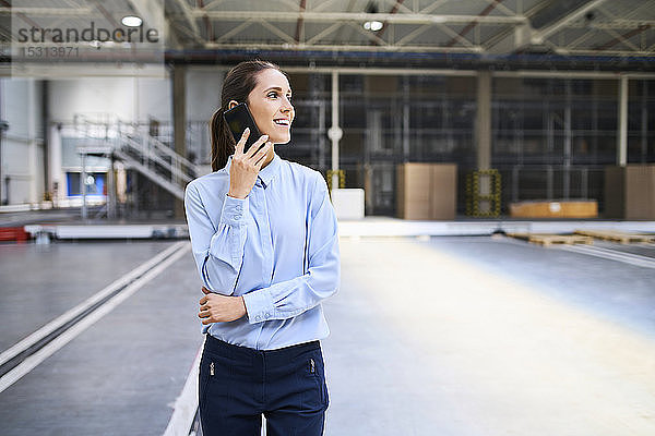 Lächelnde Geschäftsfrau am Handy in einer Fabrik