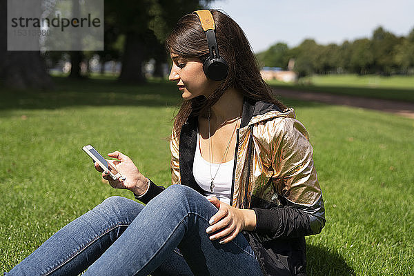 Porträt einer jungen Frau  die eine glänzende Jacke trägt und ein Smartphone und Kopfhörer benutzt