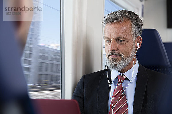 Älterer Geschäftsmann im Zug sitzend  mit Kopfhörern