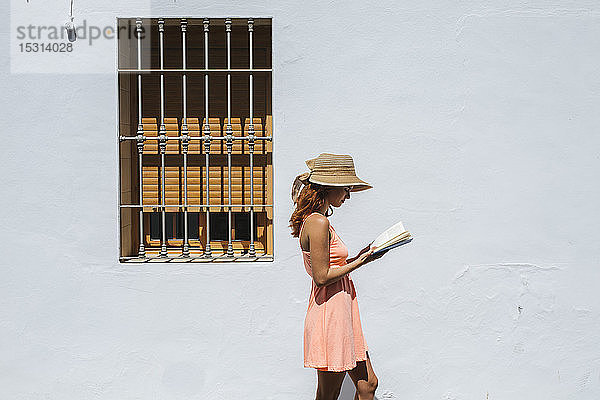 Rothaarige junge Frau liest vor einem Haus ein Buch  Frigiliana  Málaga  Spanien