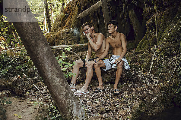Zwei barbusige Freunde rauchen in der Natur einen Joint Marihuana