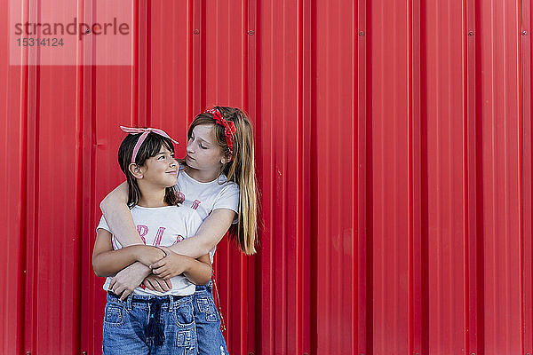 Zwei Schwestern stehen vor einer roten Wand  von Angesicht zu Angesicht