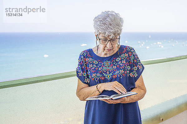 Ältere Frau liest ein Buch auf einer Terrasse