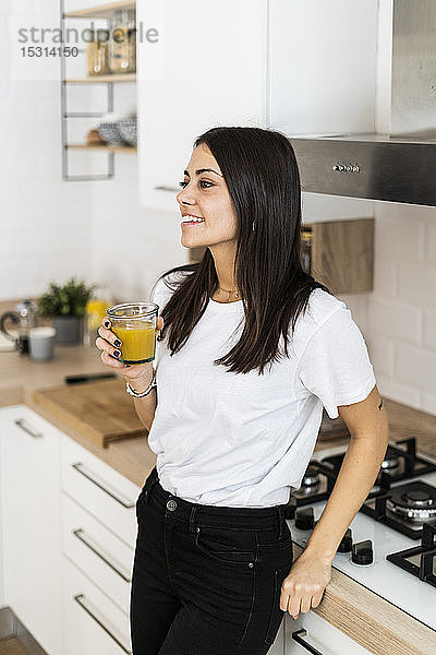 Junge Frau trinkt zu Hause in der Küche ein Glas Orangensaft