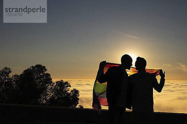 Silhouette eines schwulen Paares mit der Fahne von Gay Pride im Gegenlicht