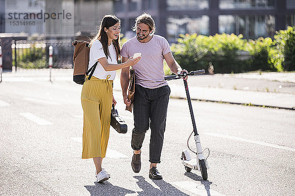 Junges Paar mit Elektroroller und Smartphone auf der Straße