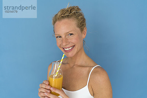 Lächelnde blonde Frau  die Saft trinkt  blauer Hintergrund
