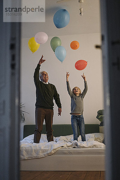 Glücklicher Grossvater und Enkel spielen zu Hause mit Luftballons auf dem Bett