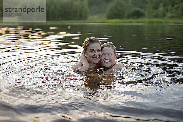Porträt einer glücklichen Mutter und eines Sohnes  die bei Sonnenuntergang in einem See baden