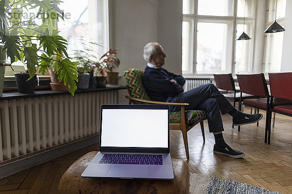 Älterer Mann zu Hause mit Laptop im Vordergrund